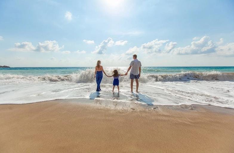 A father, a mother, and their daughter holding hands in the sand near the water